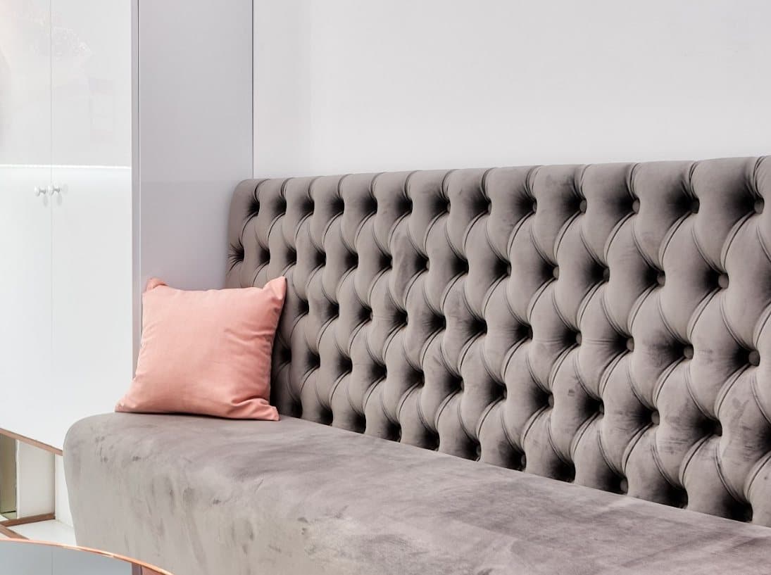 Väntrum med grå sammetssoffa, rosa kudde och kopparfärgade detaljer